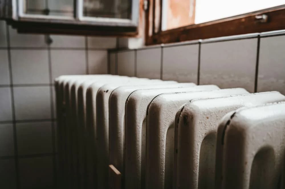 Radiateur en fonte sous une fenêtre à cadre bois, mur carrelé