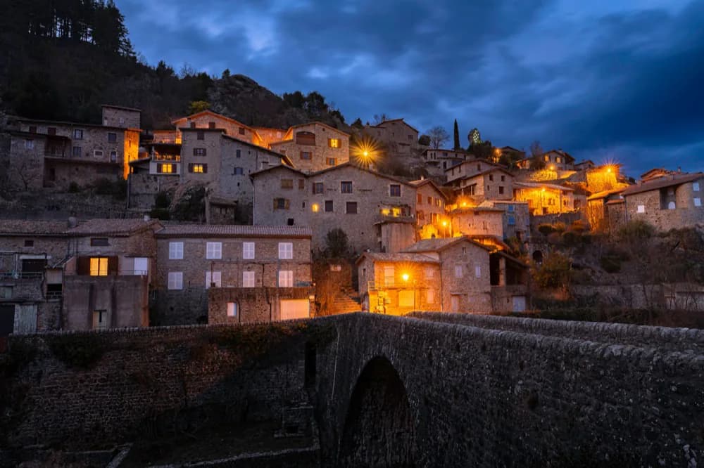 Village de pierre bâti à flanc de colline au-dessus d'un pont, au crépuscule