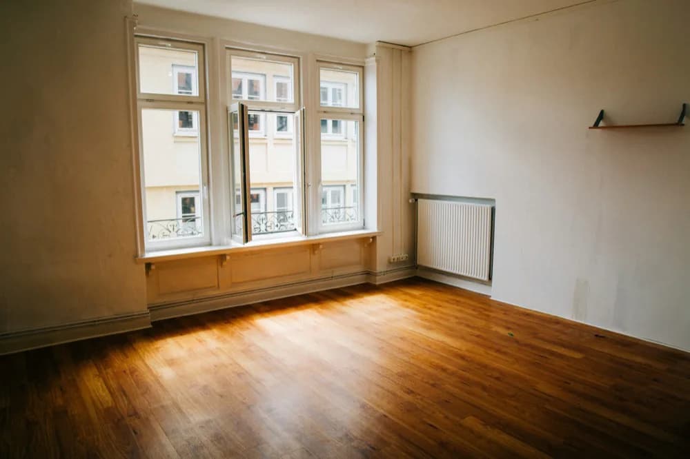 Pièce vide au parquet, fenêtres à petits carreaux et radiateur