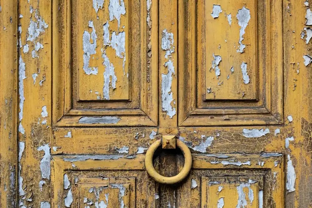Porte ancienne dont la peinture ocre se soulève par écailles